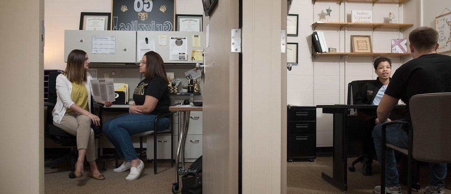 Two offices with the doors open, showing a student talking to a staff member in each office.